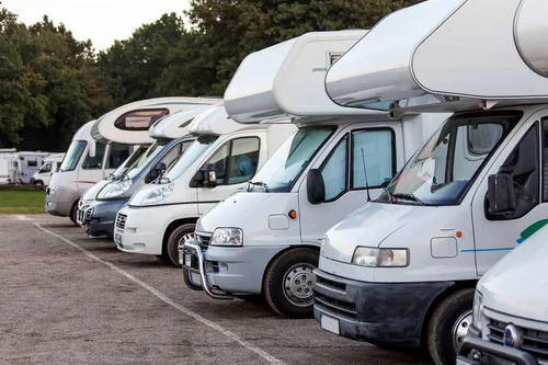 A row of white RVs parked at a campground.