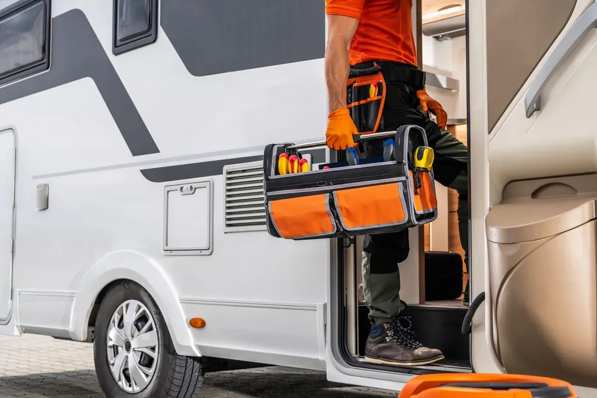 An RV technician entering a motor home with a toolbox. 