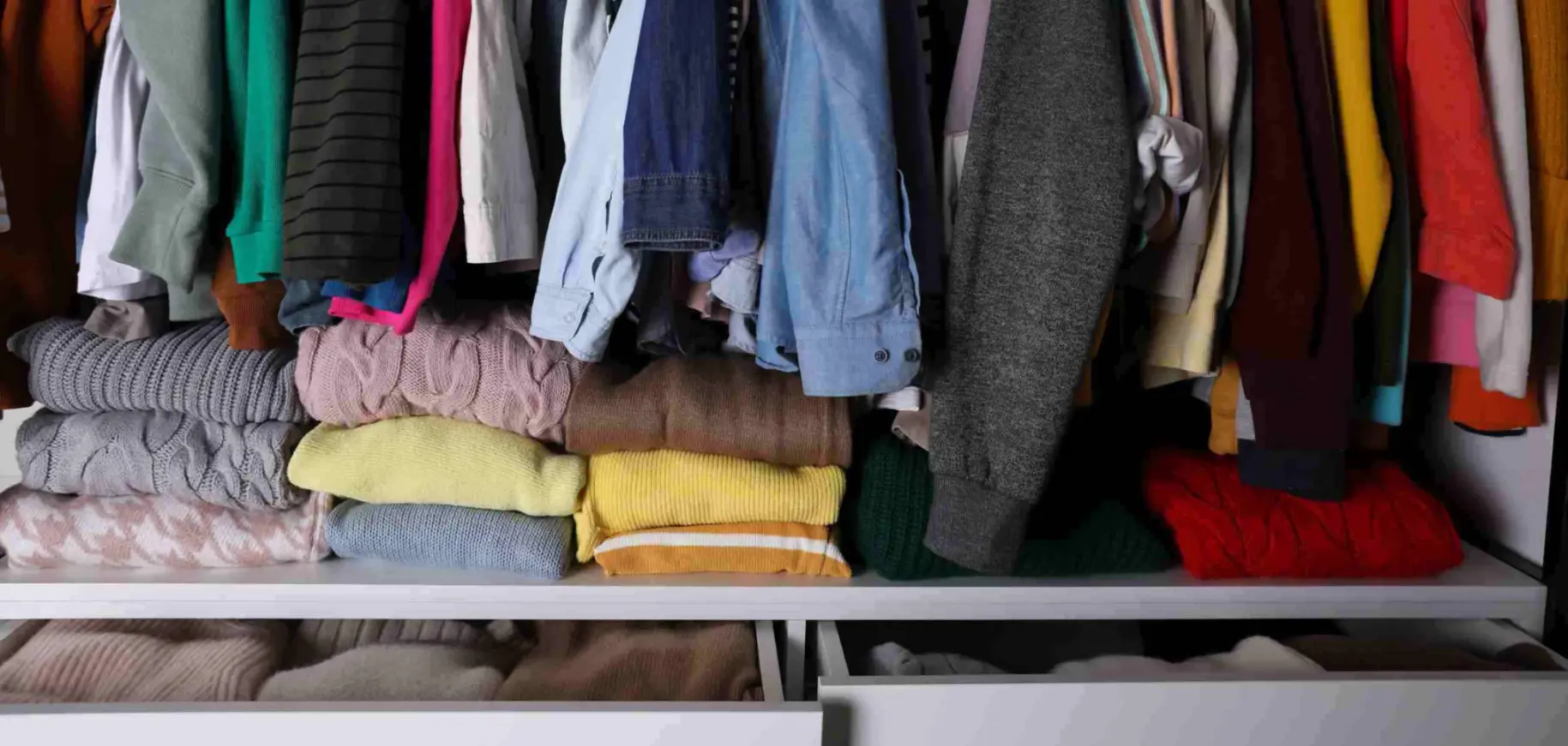 A closet stuffed with hanging clothes, folded sweaters, and drawers with garments. 