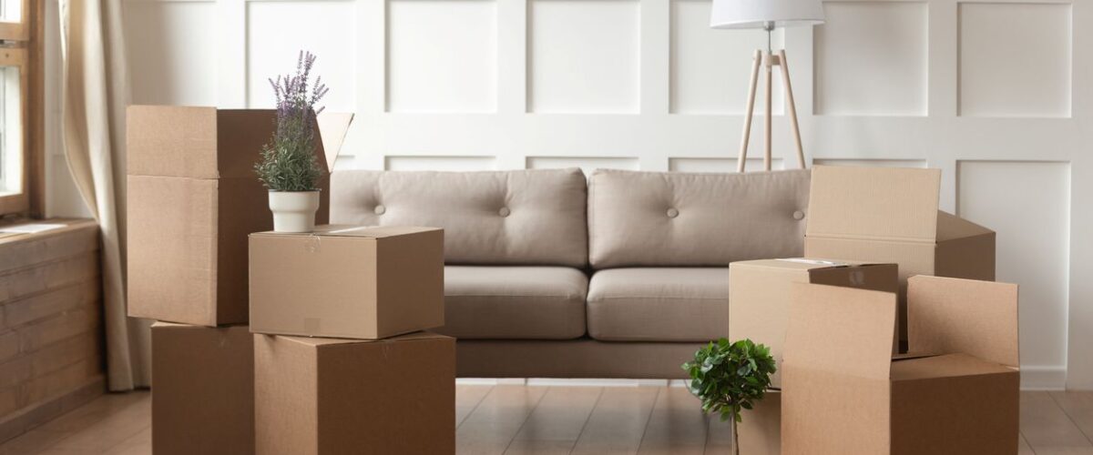 Moving boxes on a wood floor placed in front of a tan couch.