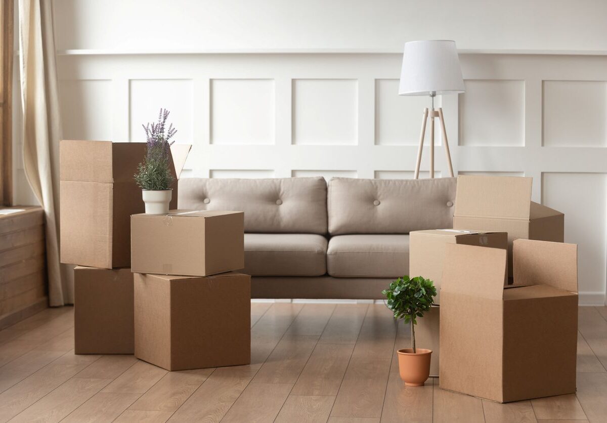 Moving boxes on a wood floor placed in front of a tan couch.