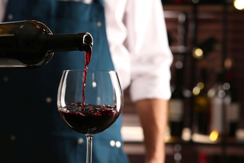 A bartender pours a glass of red wine for a customer inside a wine storage room.