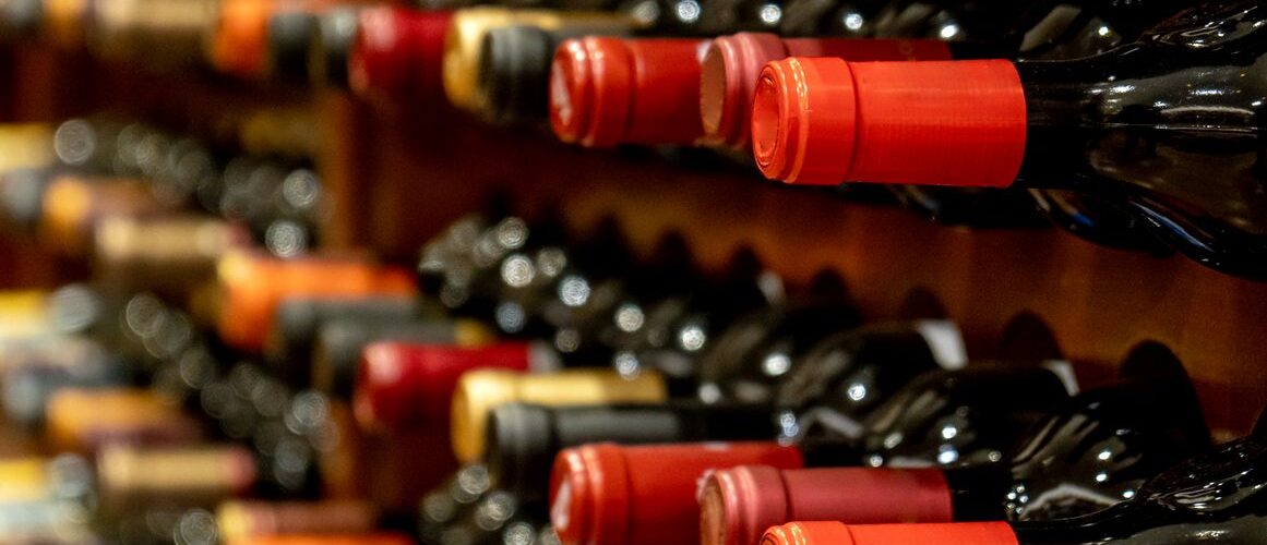 Rows of black red wine bottles sit along their wooden storage racks.