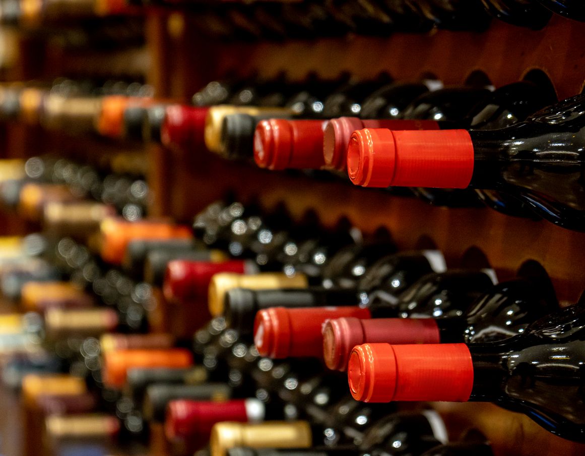 Rows of black red wine bottles sit along their wooden storage racks.