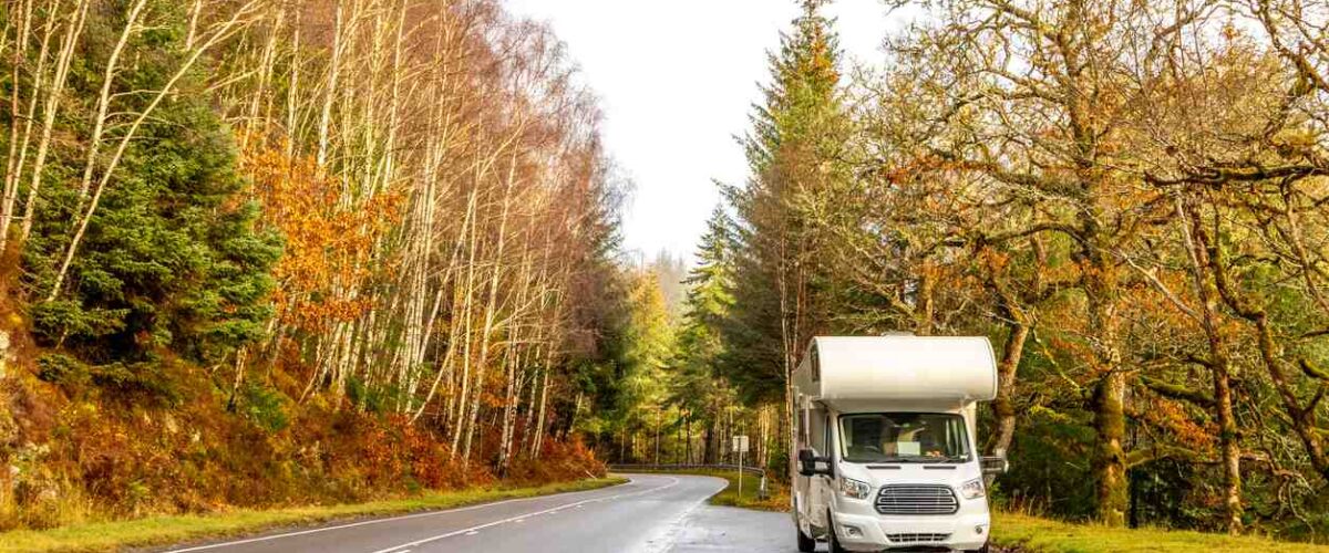 An RV on the road with beautiful fall scenery all around.