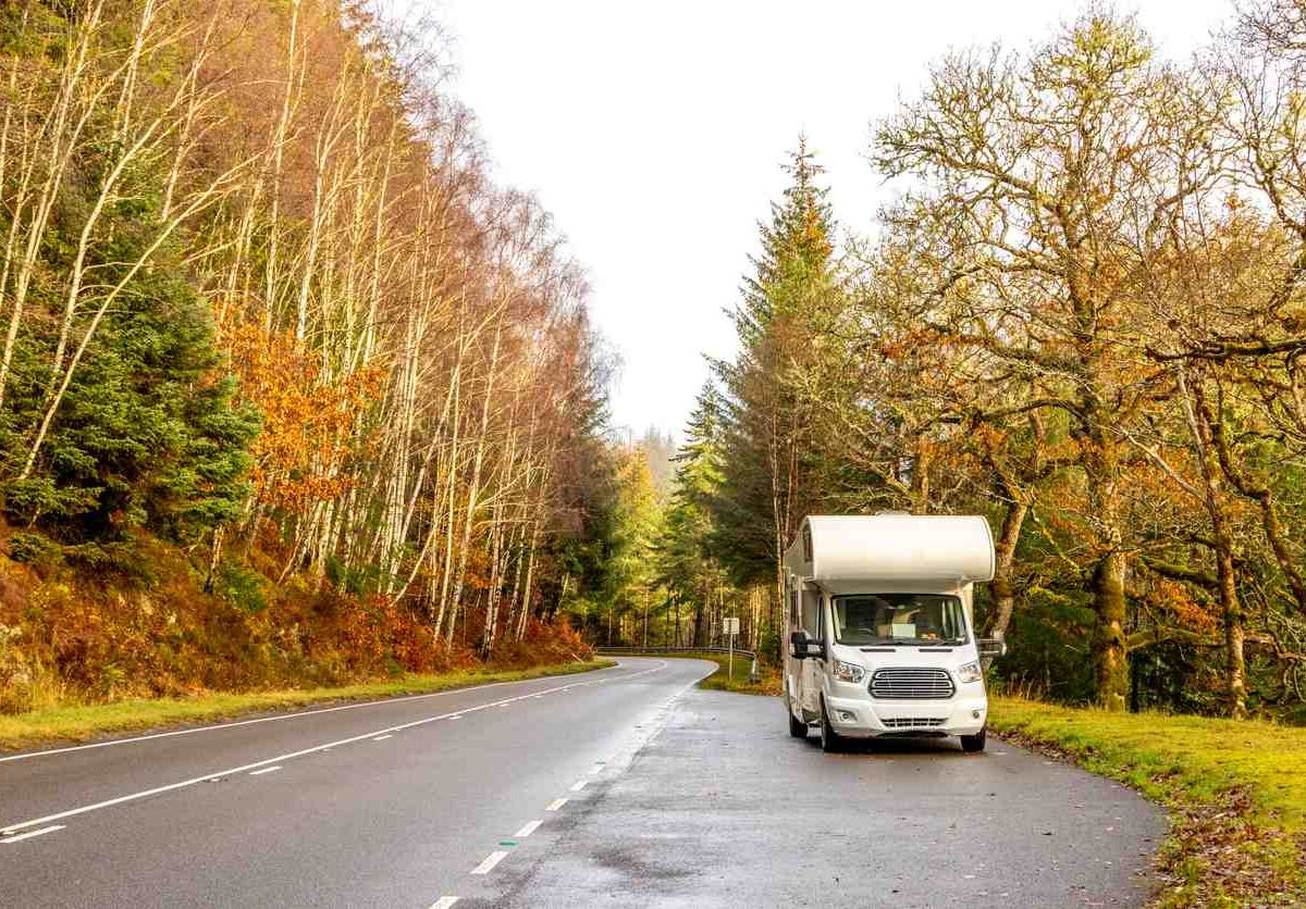 An RV on the road with beautiful fall scenery all around.