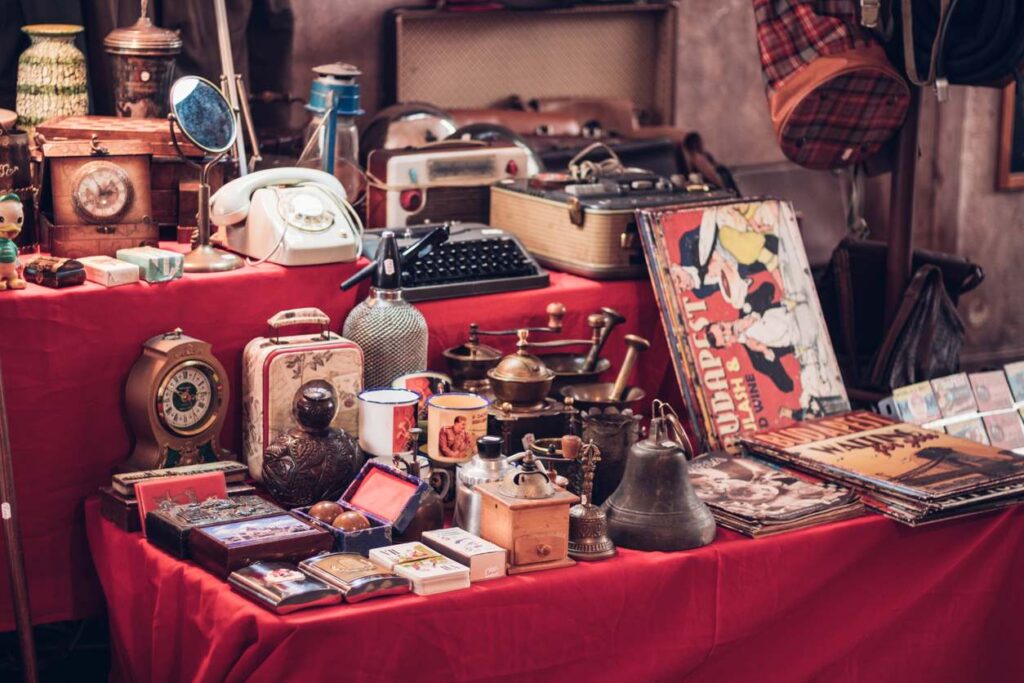 A collection of vintage items from a collection shop. Antique clocks, vinyls, and typewriters sit on top of red tables.