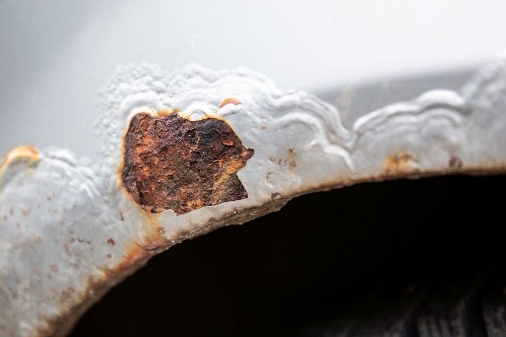 Bubbling and cracked paint with rust on the edge of a gray vehicle.